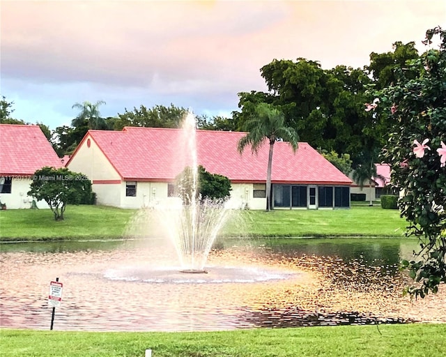 view of front of home with a tile roof, a water view, a front lawn, and stucco siding