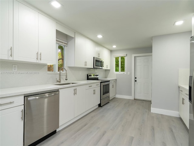 kitchen with white cabinetry, sink, light hardwood / wood-style flooring, backsplash, and appliances with stainless steel finishes