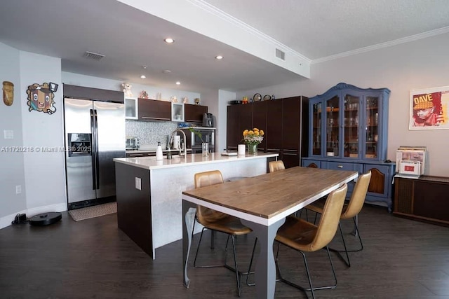 kitchen featuring decorative backsplash, stainless steel refrigerator with ice dispenser, ornamental molding, a breakfast bar, and a kitchen island with sink