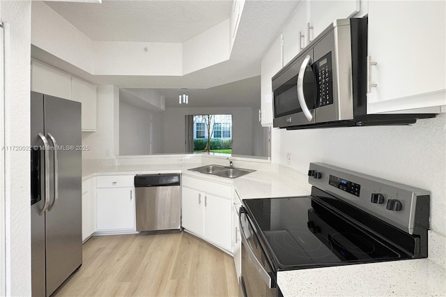 kitchen featuring appliances with stainless steel finishes, a textured ceiling, white cabinetry, sink, and light wood-type flooring