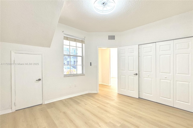 unfurnished bedroom with light wood-type flooring, a textured ceiling, and a closet