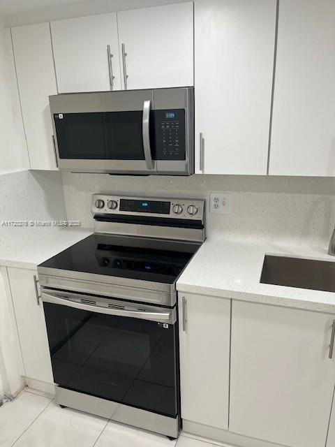 kitchen featuring backsplash, sink, light tile patterned floors, appliances with stainless steel finishes, and white cabinetry