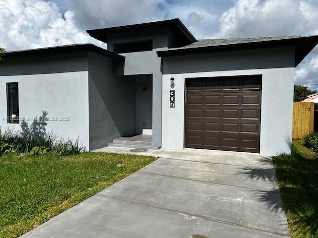 301 NW 28th Ave, Fort Lauderdale, FL 33311 - view of front of home with an attached garage, stucco siding, driveway, and a front lawn