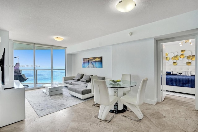 dining space featuring expansive windows, a water view, and a textured ceiling