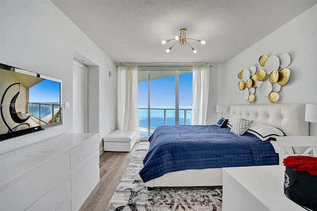 bedroom featuring a water view, light wood-type flooring, a textured ceiling, and a chandelier