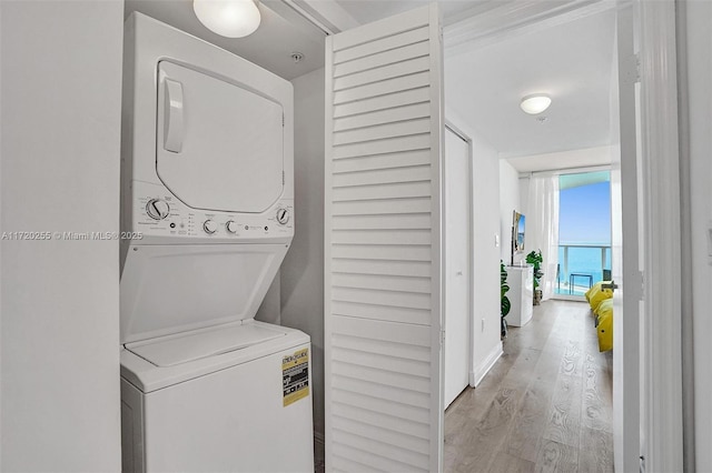 clothes washing area with light hardwood / wood-style floors and stacked washer / dryer