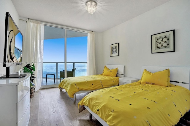 bedroom featuring access to outside, floor to ceiling windows, a water view, and light hardwood / wood-style floors