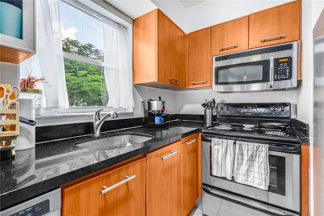 kitchen with appliances with stainless steel finishes, dark stone countertops, and sink