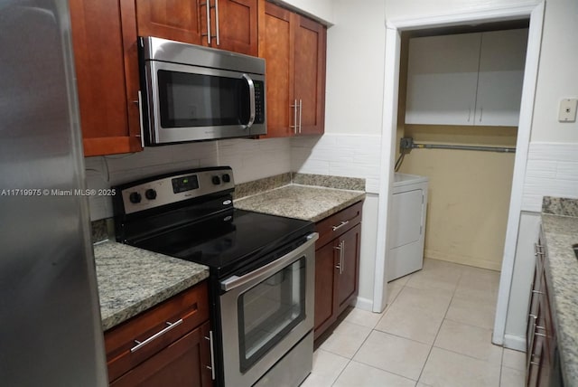 kitchen featuring washer / dryer, stone counters, light tile patterned flooring, and appliances with stainless steel finishes