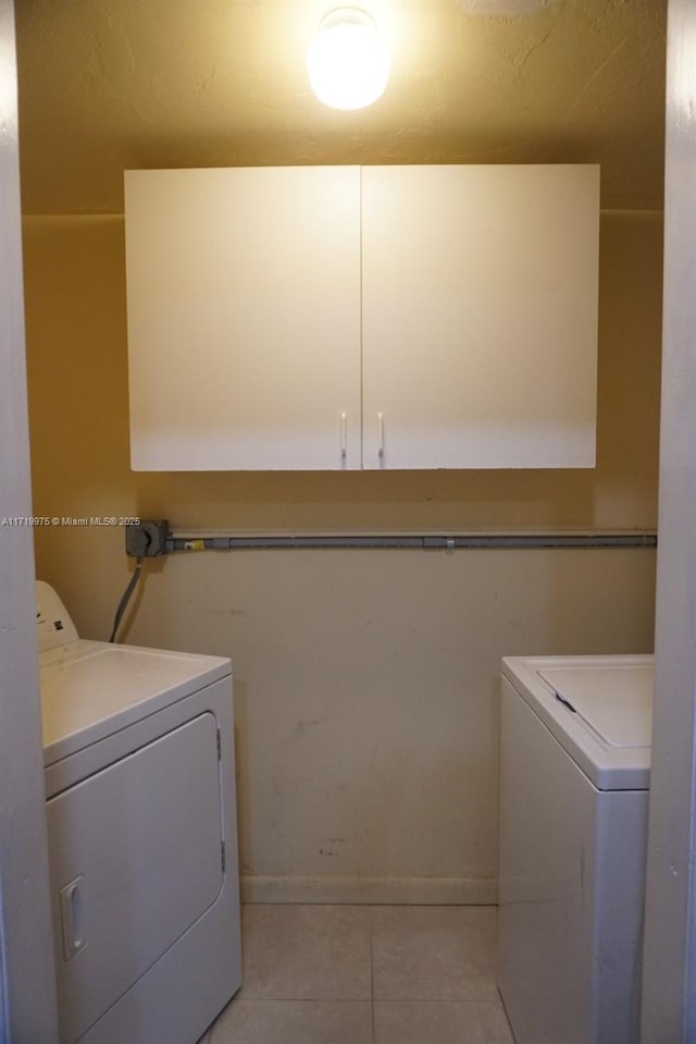 washroom with washing machine and dryer, light tile patterned floors, and cabinets