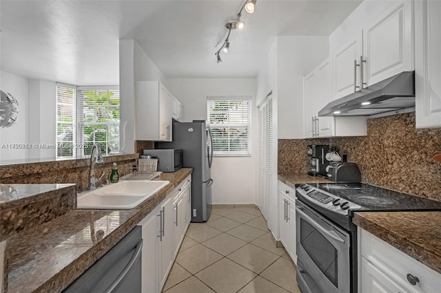 kitchen with appliances with stainless steel finishes, backsplash, sink, light tile patterned floors, and white cabinets