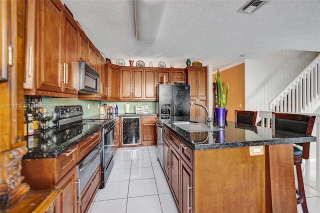 kitchen with beverage cooler, sink, black appliances, light tile patterned floors, and an island with sink