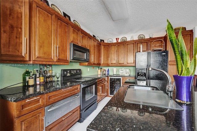 kitchen featuring dark stone counters, a textured ceiling, black appliances, light tile patterned floors, and wine cooler