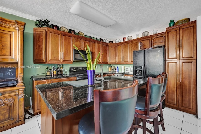 kitchen with light tile patterned floors, a textured ceiling, a kitchen island with sink, and black appliances