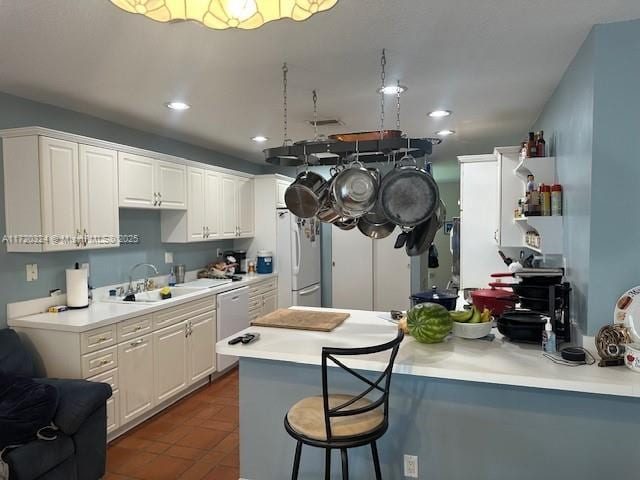 kitchen featuring kitchen peninsula, a breakfast bar, sink, white fridge, and white cabinetry