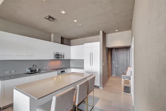 kitchen with a kitchen bar, black electric cooktop, sink, white cabinets, and a center island