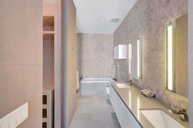 bathroom featuring vanity, a bath, tile walls, tile patterned flooring, and toilet