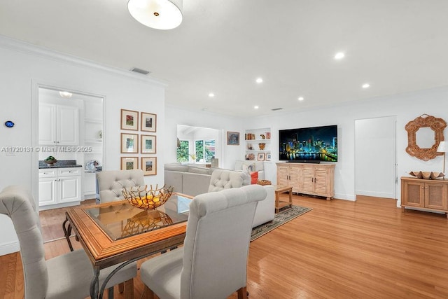 dining room featuring built in shelves, crown molding, and light hardwood / wood-style flooring