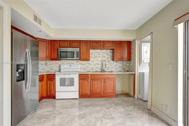 kitchen featuring appliances with stainless steel finishes, backsplash, a textured ceiling, sink, and stacked washer and clothes dryer