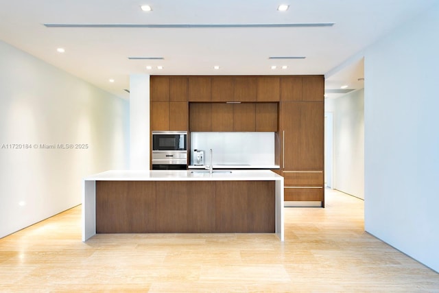 kitchen with a large island, sink, oven, and light wood-type flooring