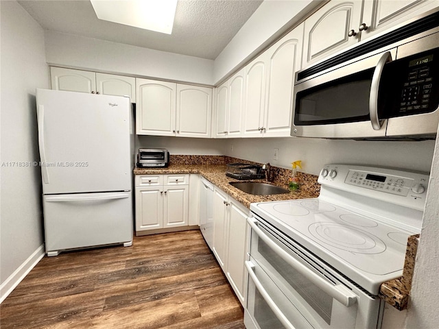 kitchen featuring white appliances, dark wood-type flooring, sink, dark stone countertops, and white cabinetry