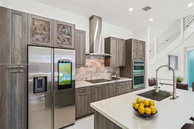 kitchen with sink, wall chimney range hood, tasteful backsplash, light tile patterned floors, and appliances with stainless steel finishes