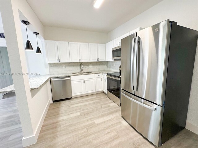 kitchen featuring white cabinetry, stainless steel appliances, sink, hanging light fixtures, and backsplash