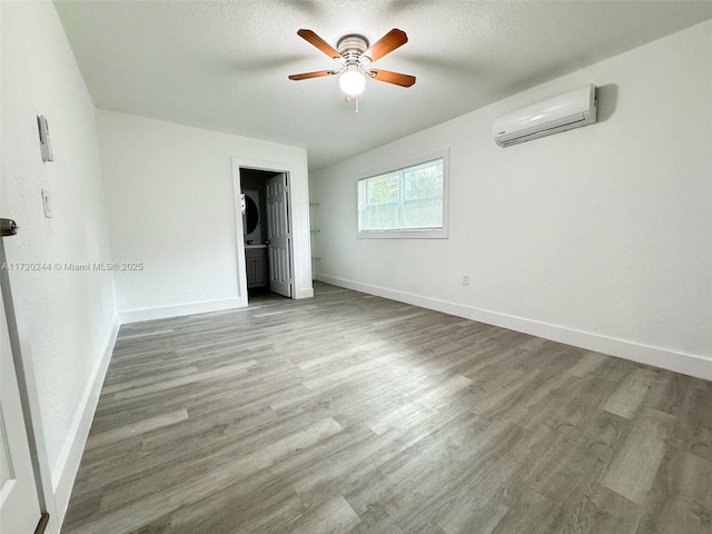 unfurnished bedroom with a wall unit AC, stacked washer and dryer, ceiling fan, a textured ceiling, and light hardwood / wood-style flooring