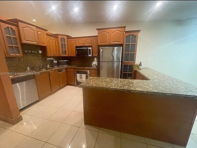 kitchen with stainless steel appliances, kitchen peninsula, dark stone countertops, decorative backsplash, and light tile patterned floors