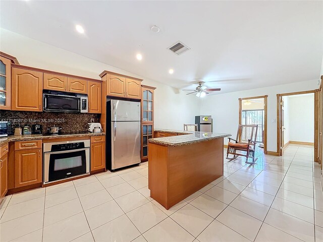 kitchen with appliances with stainless steel finishes, light tile patterned floors, light stone counters, and decorative backsplash