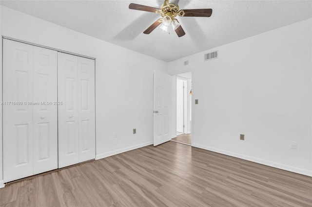 unfurnished bedroom featuring ceiling fan, a closet, a textured ceiling, and light wood-type flooring