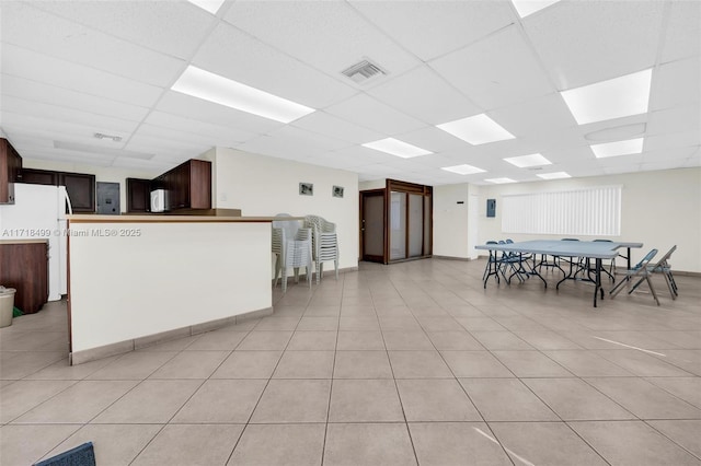 interior space with white appliances, light tile patterned floors, a paneled ceiling, and dark brown cabinetry