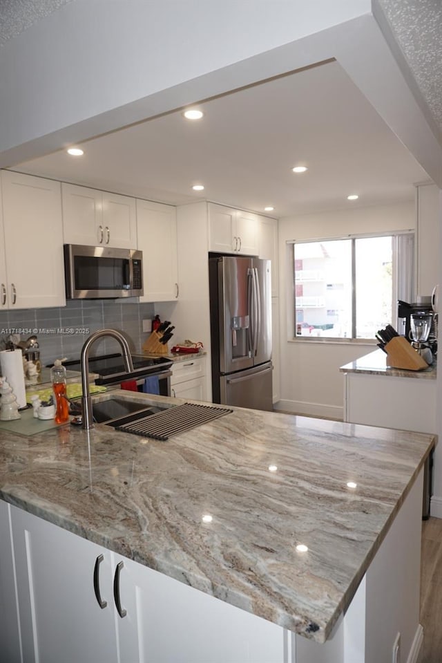 kitchen with kitchen peninsula, light stone countertops, white cabinets, and appliances with stainless steel finishes