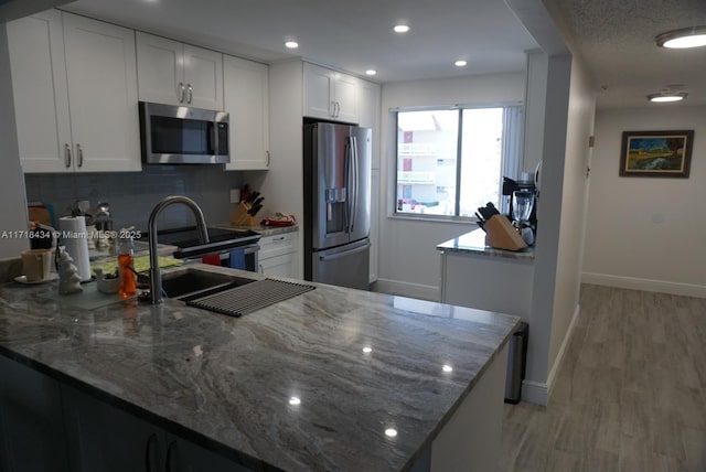 kitchen with dark stone countertops, white cabinetry, stainless steel appliances, and decorative backsplash