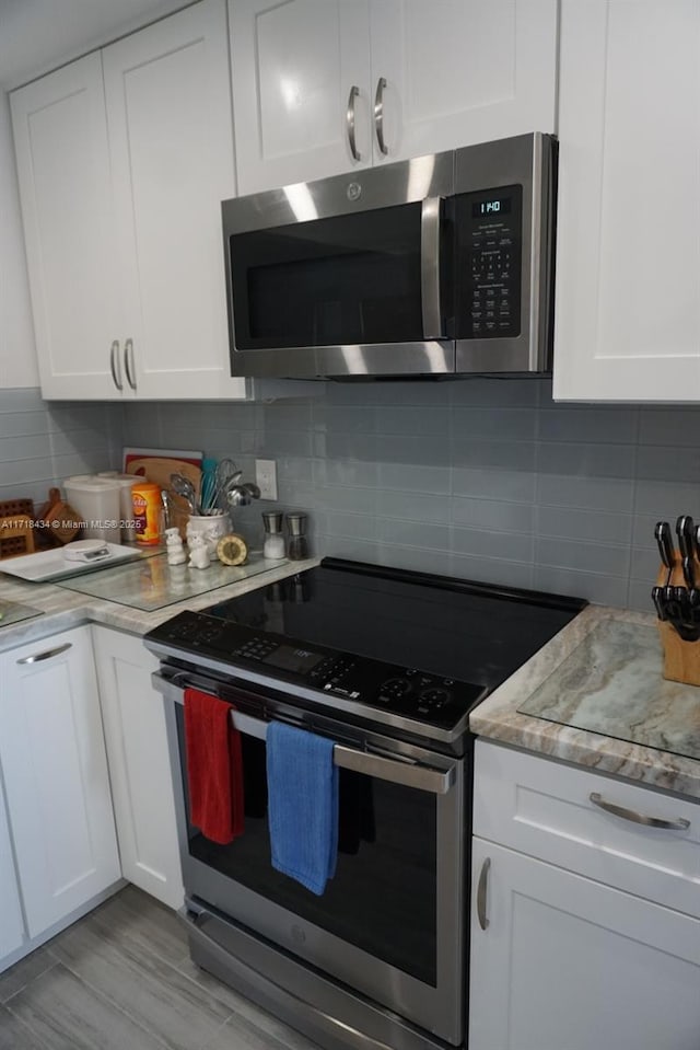 kitchen with tasteful backsplash, white cabinets, and appliances with stainless steel finishes