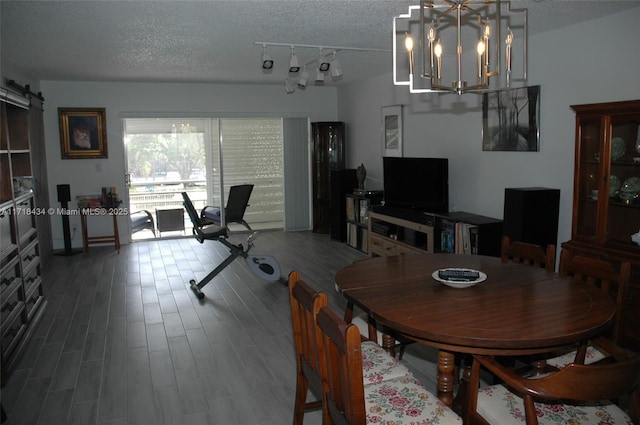 dining space featuring a barn door, a textured ceiling, wood finished floors, and an inviting chandelier