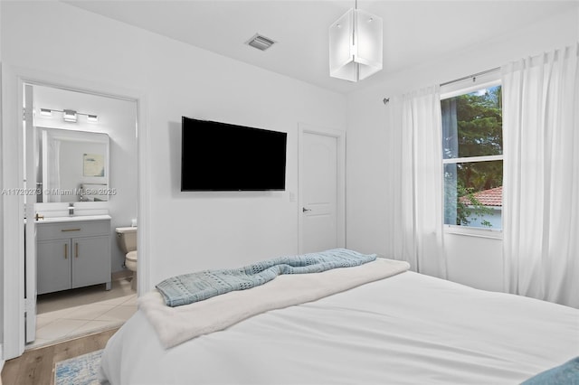 bedroom with light wood-type flooring, sink, and connected bathroom