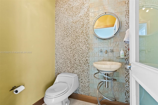 bathroom featuring toilet, tile walls, and sink