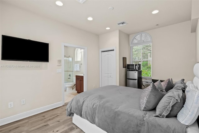 bedroom featuring stainless steel refrigerator, ensuite bath, a closet, and light hardwood / wood-style flooring