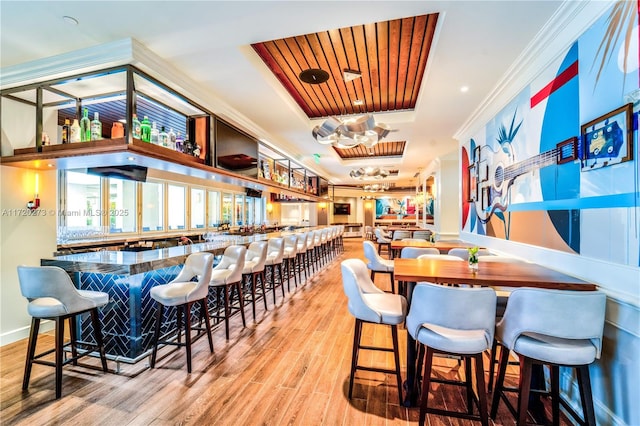 bar featuring a raised ceiling, crown molding, and light hardwood / wood-style flooring