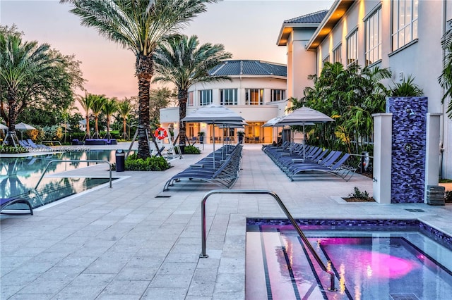 pool at dusk with a community hot tub and a patio