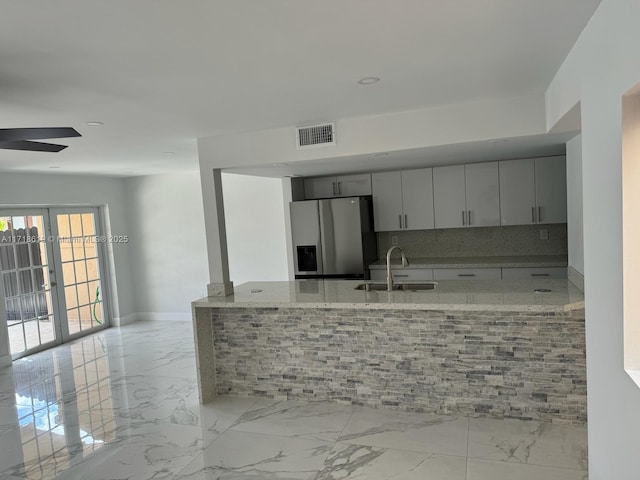 kitchen featuring ceiling fan, sink, tasteful backsplash, stainless steel fridge with ice dispenser, and light stone counters