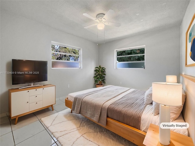 bedroom featuring ceiling fan, light tile patterned floors, and a textured ceiling