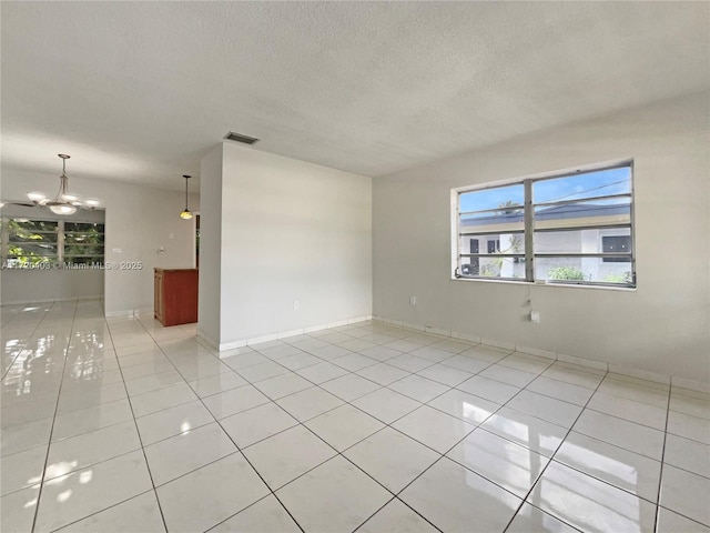 unfurnished room featuring light tile patterned flooring, a textured ceiling, and an inviting chandelier