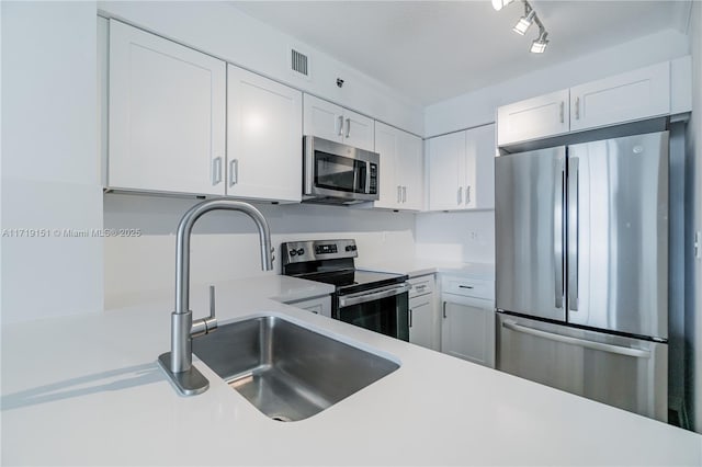 kitchen with white cabinets, appliances with stainless steel finishes, rail lighting, and sink