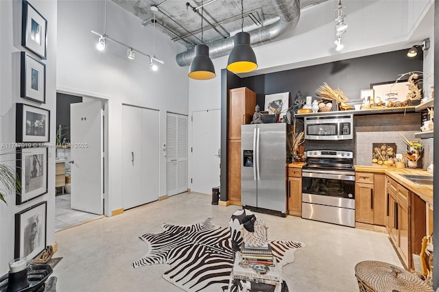 kitchen featuring a towering ceiling, stainless steel appliances, and decorative light fixtures