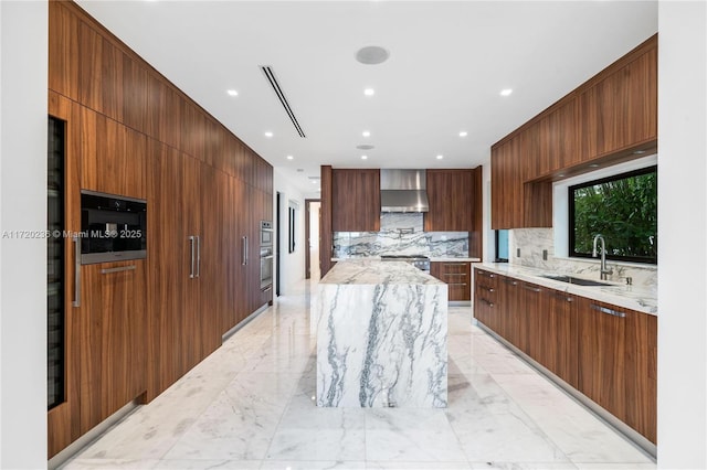 kitchen featuring decorative backsplash, sink, light stone countertops, and wall chimney range hood