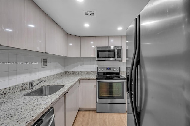 kitchen featuring backsplash, sink, appliances with stainless steel finishes, light hardwood / wood-style floors, and light stone counters