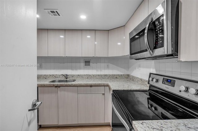 kitchen featuring black electric range oven, sink, light stone countertops, and backsplash