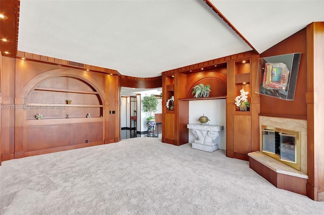 unfurnished living room featuring built in shelves, light colored carpet, and wooden walls